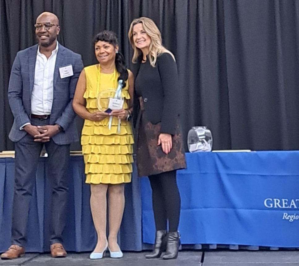 Three people at awards ceremony stage — Community Impact Award